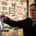 "A photo-realistic image depicting a Polish voter in front of discarded propaganda posters, some with Russian symbols, highlighting the theme of Russian interference in the Polish election. The voter is about to cast a ballot, symbolizing resilience against external influence.