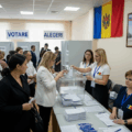 People voting in a polling station in Moldova with a picture of Vladimir Putin and Russian soldiers behind them illustrating Russian influence on the elections