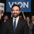 zohran mamdani standing in front of cheering supporters after being endorsed for a mayor of New York City and part of the new green alliance in the us